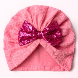 Detail of pink knitted baby turban hat with shiny magenta sequin bow decoration