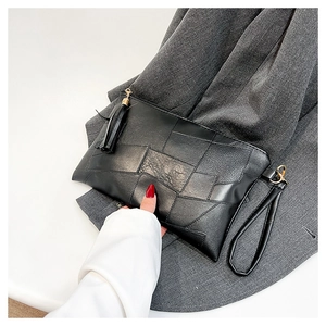 Detail of a black leather clutch bag with geometric stitching, tassel, and wrist strap