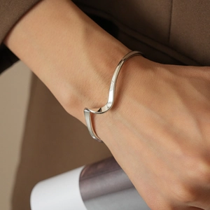 Close-up of wavy minimalist silver metal open bangle worn on wrist with sleek finish