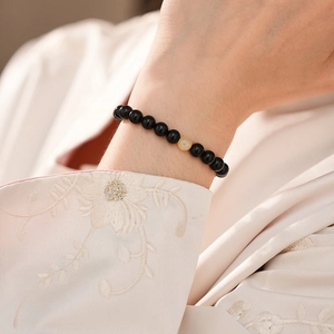 Detail of beaded black obsidian bracelet with amber accent worn on wrist with silk sleeve