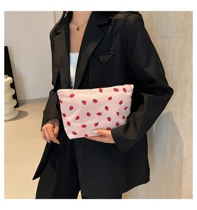 Detailed strawberry embroidery on pink corduroy tote bag held by a model in a suit