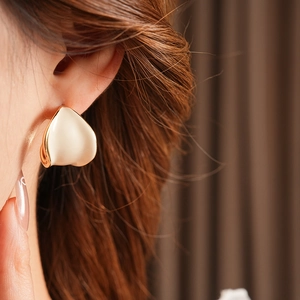 Dettaglio di un orecchino a cerchio a C in smalto beige indossato da una modella con luce naturale