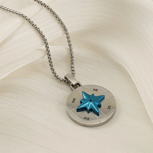 Silver stainless steel compass star necklace with blue accents on textured satin background