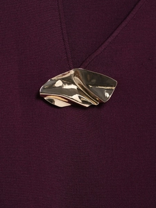 Detail of artistic wavy gold metal accessory on premium dark purple knit fabric