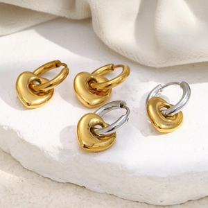 Détail de boucles d'oreilles cœur en or 18K et argent sur un socle en pierre blanche