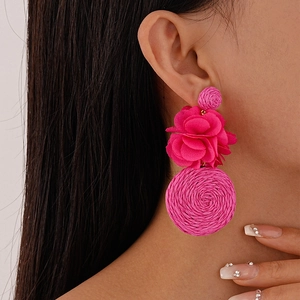 Close-up of bright pink bohemian drop earrings with woven spheres and fabric flowers