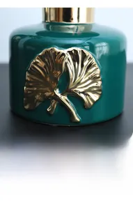 Macro detail of dark green ceramic vase featuring golden ginkgo leaf relief and gold rim