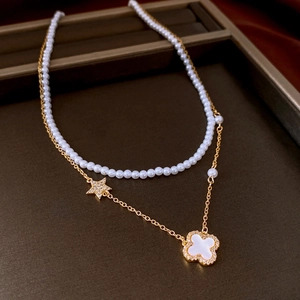 Detail of double-layer pearl necklace with gold star and clover floral pendant charm