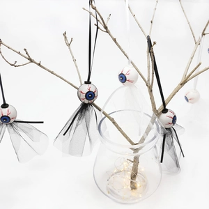 Ghost eye ornaments with black and white mesh hanging on branches for Halloween decor
