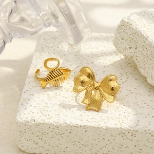 Detail of 18K gold-plated bow and fishbone rings with zircons on white stone base