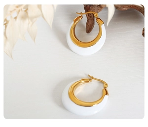 Detail of C-shaped gold hoops with white enamel finish on a minimalist wooden background