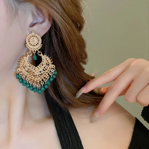 Detail of ethnic hollow teardrop earrings with gold metal and green bead fringe accents