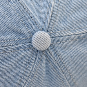 Macro shot of light blue washed denim baseball cap top button and detailed stitching