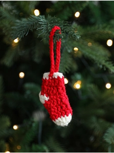 Close-up of handmade red and white knitted Christmas sock ornament on a festive tree