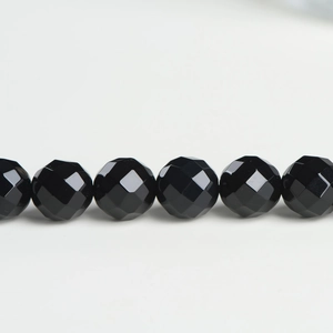 Macro view of multi-faceted black agate beads showing reflective diamond-cut texture