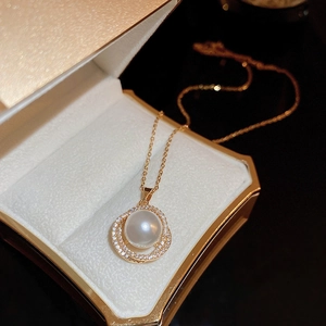 Gros plan d'un pendentif perle dorée avec anneaux en zircon dans un écrin