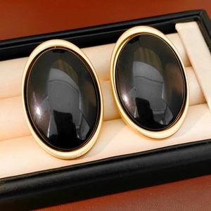 Detail of oval black resin earrings with gold-plated metal edges on a satin lining