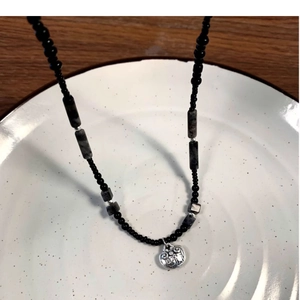 Bamboo style silver Ruyi lock pendant necklace with black beaded chain on ceramic plate