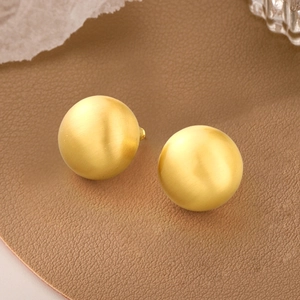 Matte gold sphere stud earrings in brushed 925 silver shown on a brown leather surface