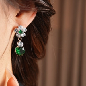 Close-up of flower stud earrings with green gemstones and sparkling cubic zirconia