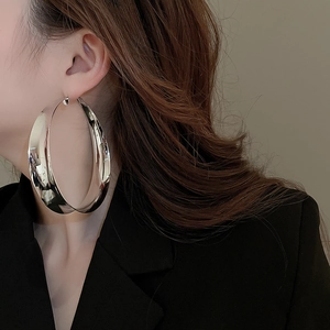 Close-up of a large silver hoop earring worn by a model in a black suit with minimalist style