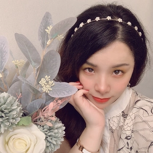 Dettaglio di un sottile cerchietto dorato con fiori bianchi e strass su una modella