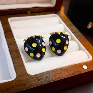 Macro detail of strawberry earrings with black enamel and gold leaves in a wooden box