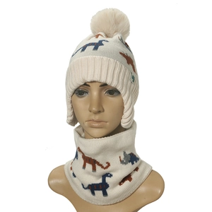 Detail of cream knitted baby hat and scarf set featuring colorful dinosaur patterns