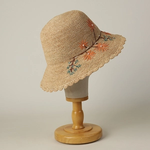 Detail of raffia hat featuring orange flower embroidery and scattered pearl accents