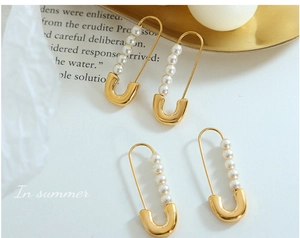 Detailed close-up of gold paperclip earrings with five white pearls on vintage books