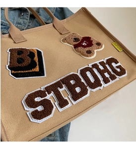 Close-up of khaki canvas tote bag featuring teddy bear embroidery and fuzzy patches