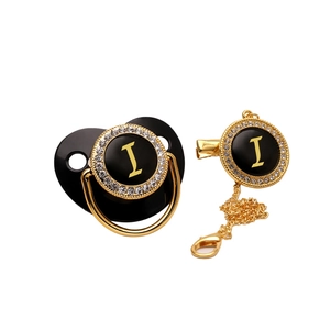 Detail of black and gold baby pacifier with rhinestone-encrusted letter I and clip chain