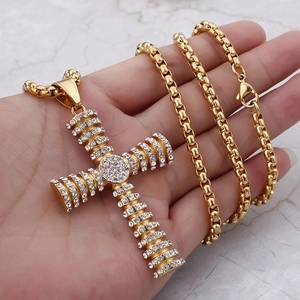 Detail of gold hip hop cross pendant with clear rhinestones on a box chain held by hand