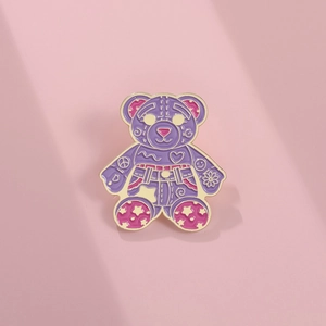 Detail of purple cartoon bear enamel pin with gold plating and colorful star patterns