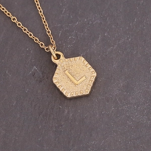 Detailed close-up of golden hexagonal pendant featuring letter L on stone background