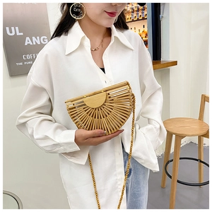 Woman holding a semi-circular woven bamboo bag with wooden bead chain in a cafe setting