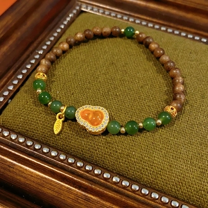 Detailed close-up of orange garnet gourd and green jade bead bracelet on vintage green velvet