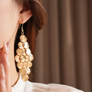 Close-up of golden multi-layer round sequin tassel earrings worn by a model