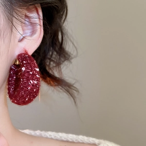 Nahaufnahme eines tiefroten, gestrickten Woll-Ohrrings, getragen von einem Modell