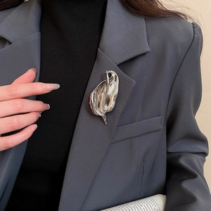Macro detail of a silver leaf-shaped liquid metal brooch on a grey suit lapel