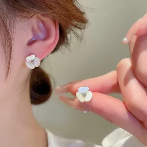 Gros plan de boucles d'oreilles fleur en perle avec pétales blancs et bordure dorée
