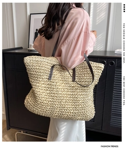 Detail of hand-woven straw tote bag with brown leather strap worn by a model