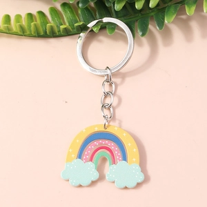 Detail of a rainbow acrylic keychain with blue clouds on a soft pink surface