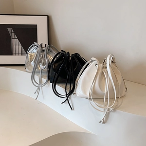 Three minimalist drawstring bucket bags in silver, black, and white on a display stand