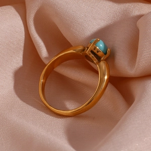 Detailed close-up of 18K gold petal ring with turquoise stone on soft pink silk