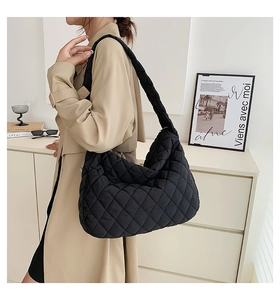 Detail of a black quilted puffer tote bag worn on the shoulder with casual outerwear