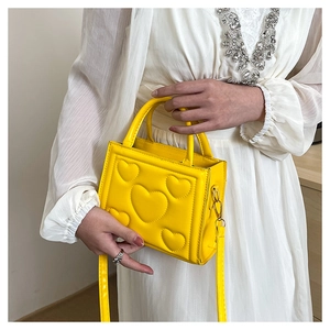 Détail d'un sac à main jaune en cuir PU avec motif cœur gaufré et bandoulière assortie