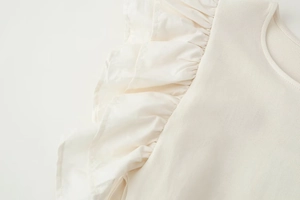 Close-up of cream ribbed knit fabric with delicate ruffled edge detailing on the sleeve