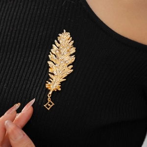 Close-up of a gold feather brooch with crystals and F-logo charm on black sweater
