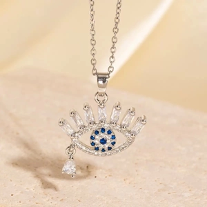 Silver Evil Eye necklace with blue zircon and eyelash details on beige stone surface